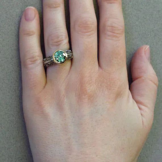 Gold-plated flower-shaped ring with a green gemstone on a silver-tone band, shown from above.