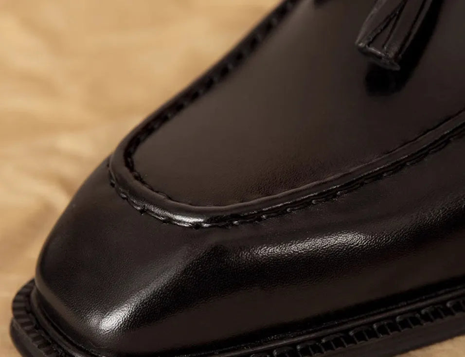Men's black and brown British-style leather slip-on loafers showing polished leather upper and rubber sole
