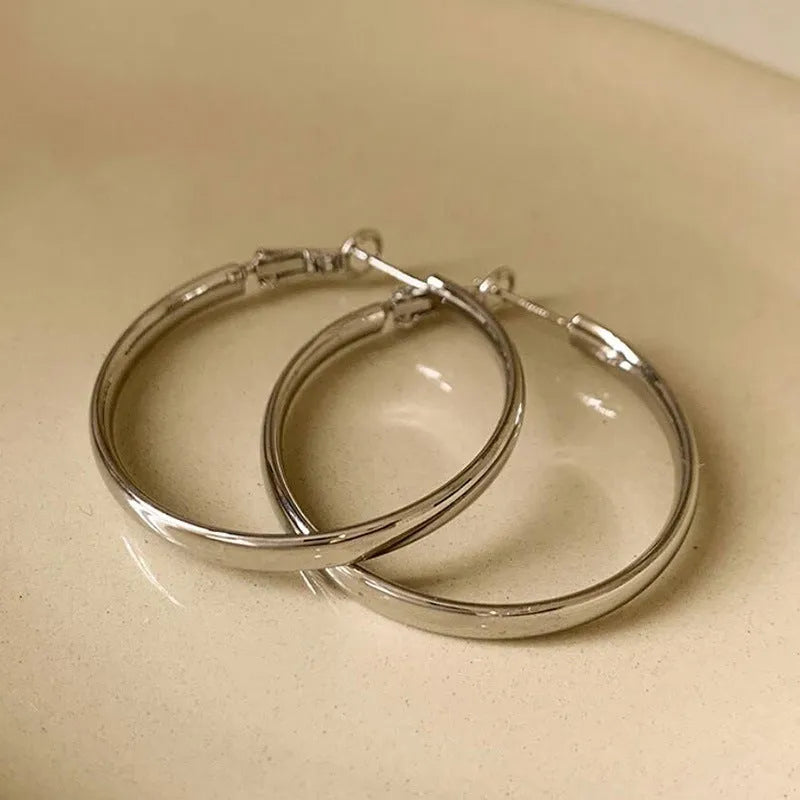 A pair of simple metal circle hoop earrings in a gold colour against a plain background.