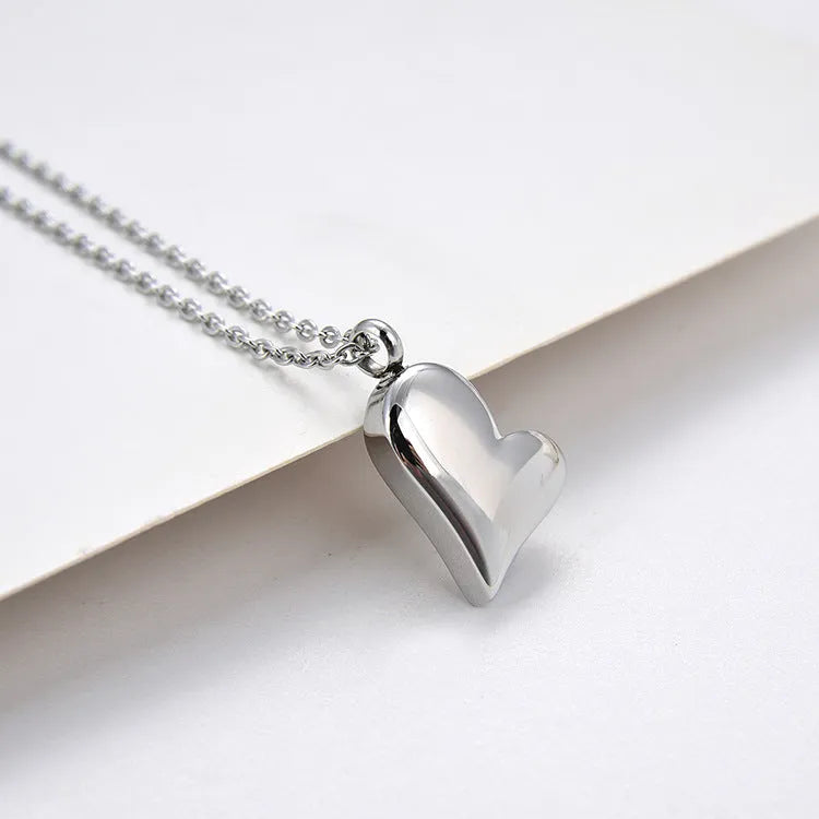 Silver curved peach heart stainless steel pendant necklace on a model, showing the adjustable chain length.