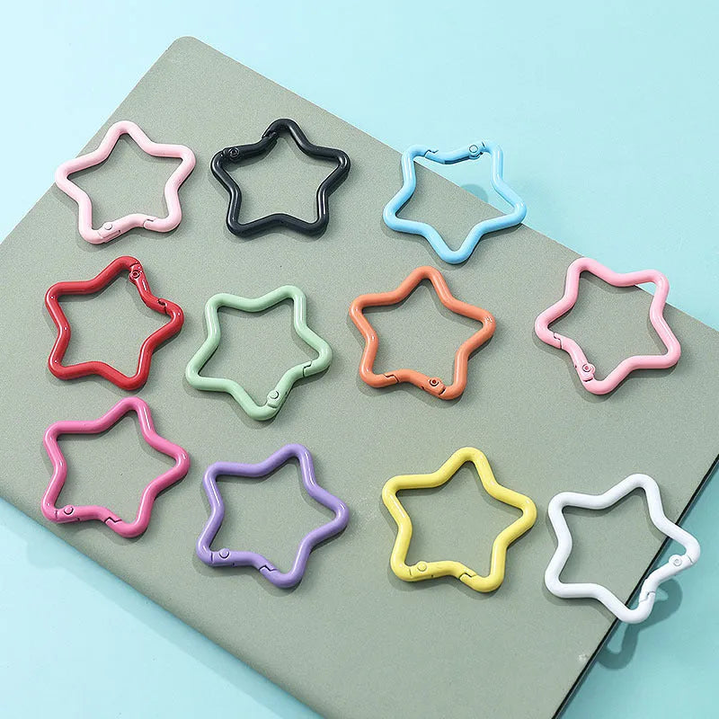 Zinc alloy five-pointed star keychain in light pink colour on a black background.
