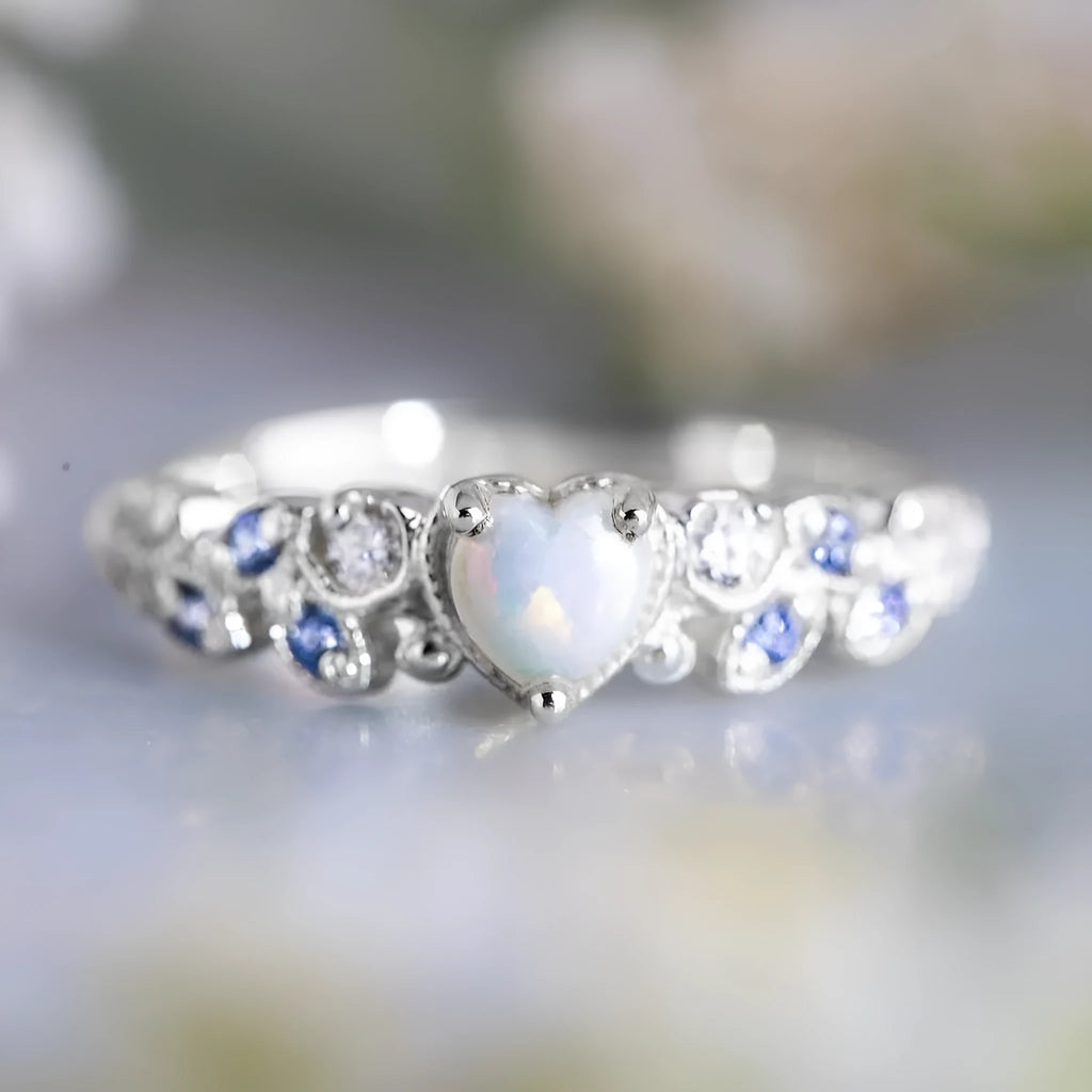White alloy women's heart ring with floral opal ocean love design on a finger.