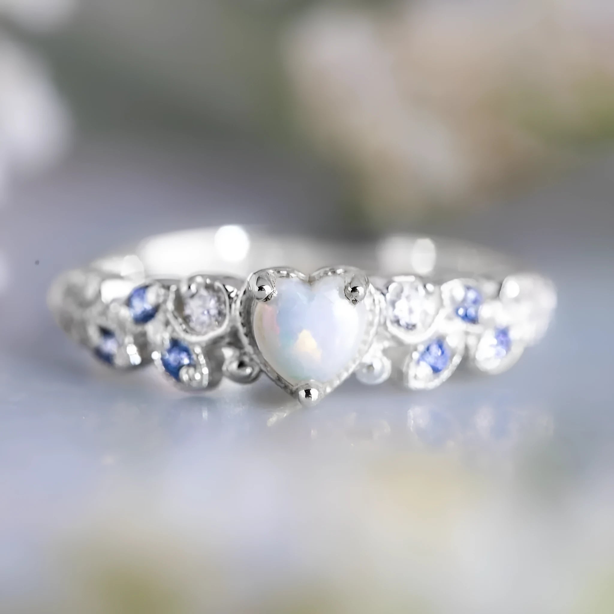 White alloy women's heart ring with floral opal ocean love design on a finger.