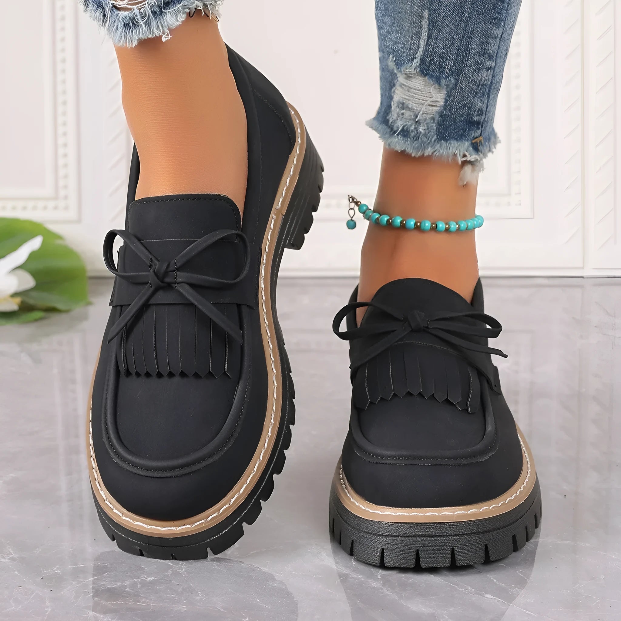 Women's black plus size loafers with tassel and bowknot detail on a chunky rubber sole.