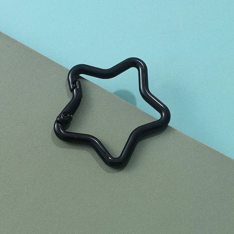Zinc alloy five-pointed star keychain in light pink colour on a black background.