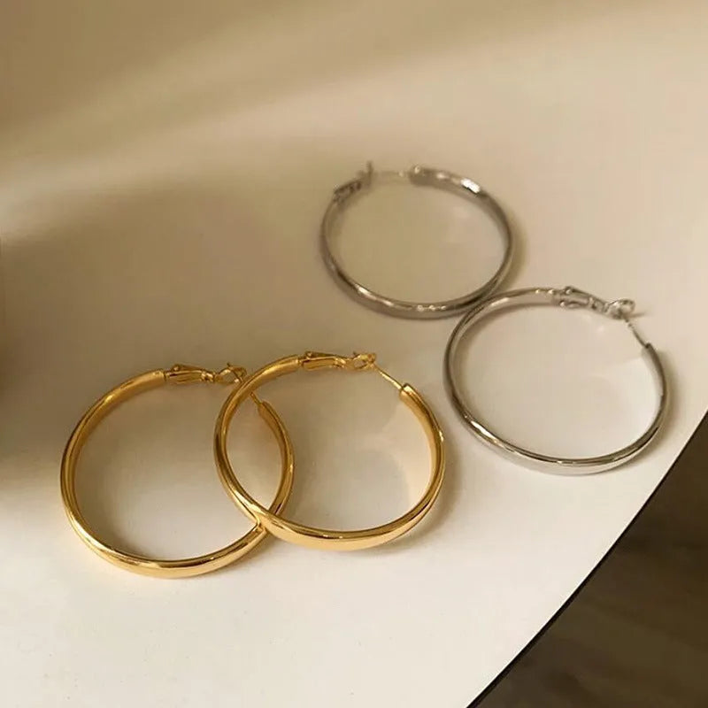 A pair of simple metal circle hoop earrings in a gold colour against a plain background.
