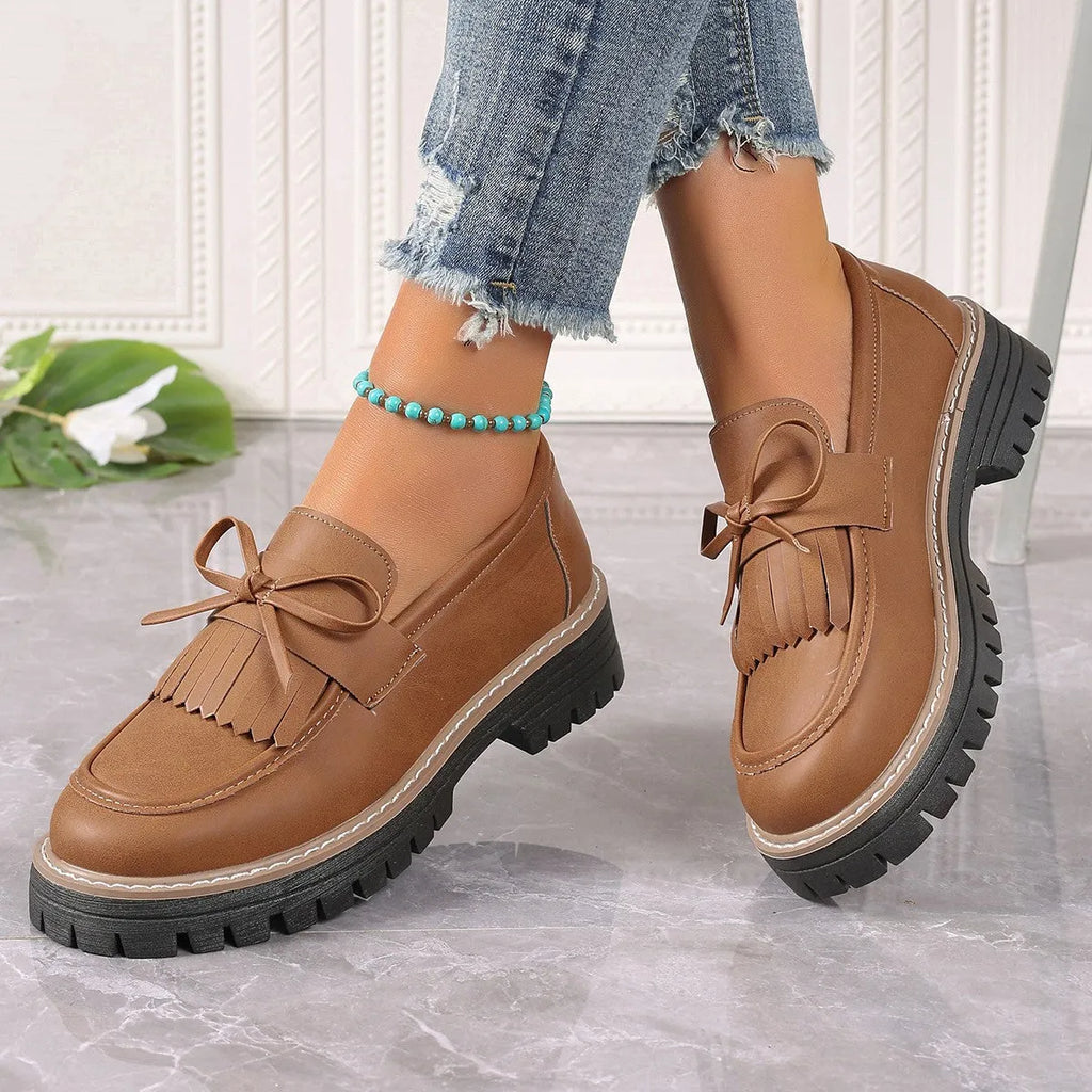 Women's black plus size loafers with tassel and bowknot detail on a chunky rubber sole.