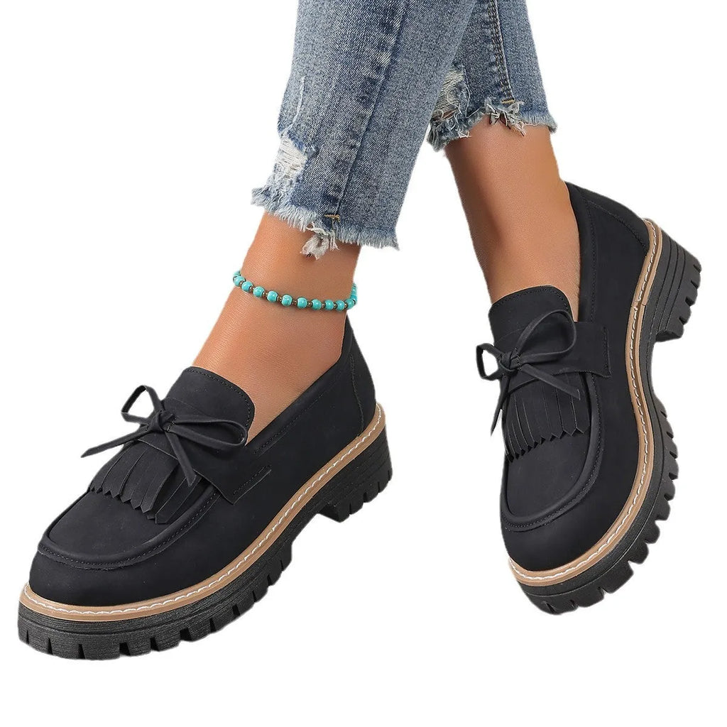Women's black plus size loafers with tassel and bowknot detail on a chunky rubber sole.