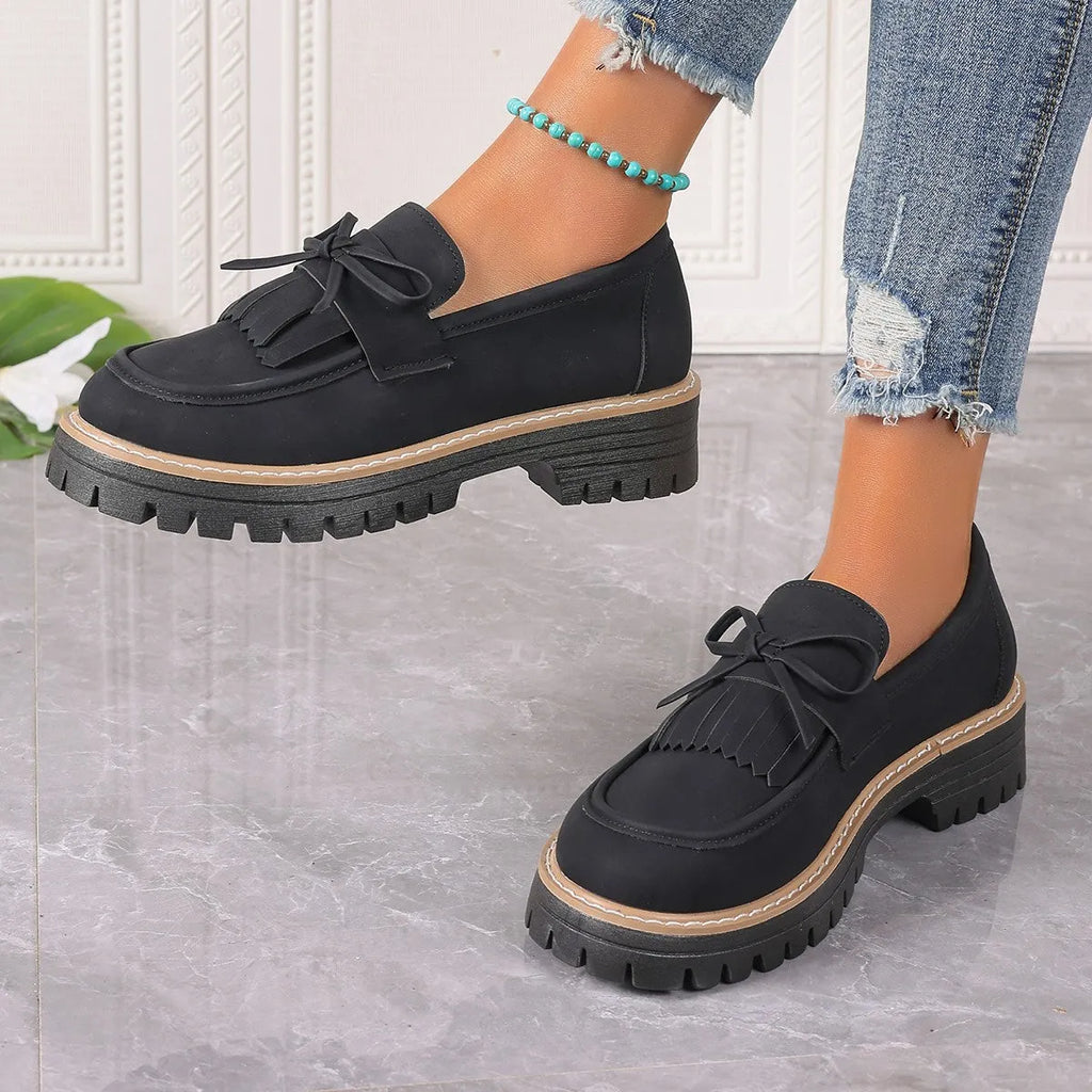 Women's black plus size loafers with tassel and bowknot detail on a chunky rubber sole.