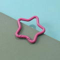 Zinc alloy five-pointed star keychain in light pink colour on a black background.