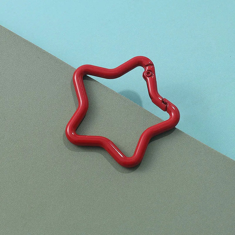 Zinc alloy five-pointed star keychain in light pink colour on a black background.