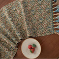 Dark blue and white striped jacquard table runner with tassel trim laid on a wooden dining table.