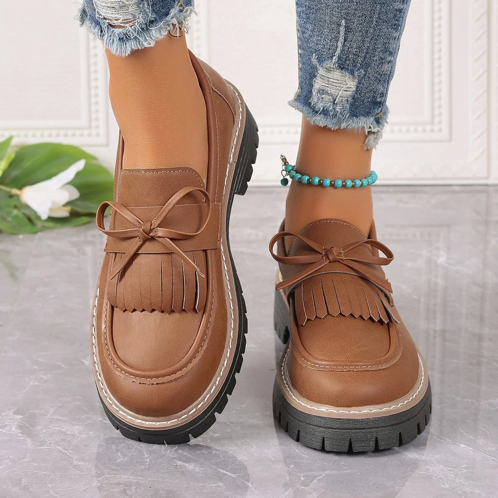 Women's black plus size loafers with tassel and bowknot detail on a chunky rubber sole.