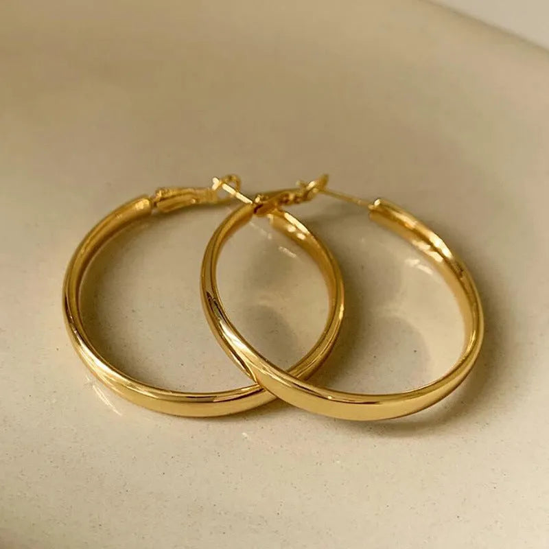 A pair of simple metal circle hoop earrings in a gold colour against a plain background.