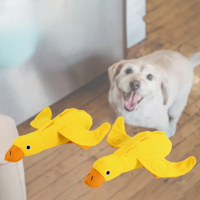 Yellow plush teddy bear dog toy with a small duck doll attached, showing food dispensing holes.