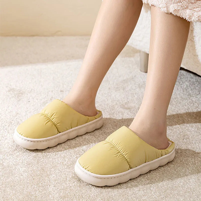 Blue down cotton indoor slippers with thick rubber sole and plush lining on a wooden floor.