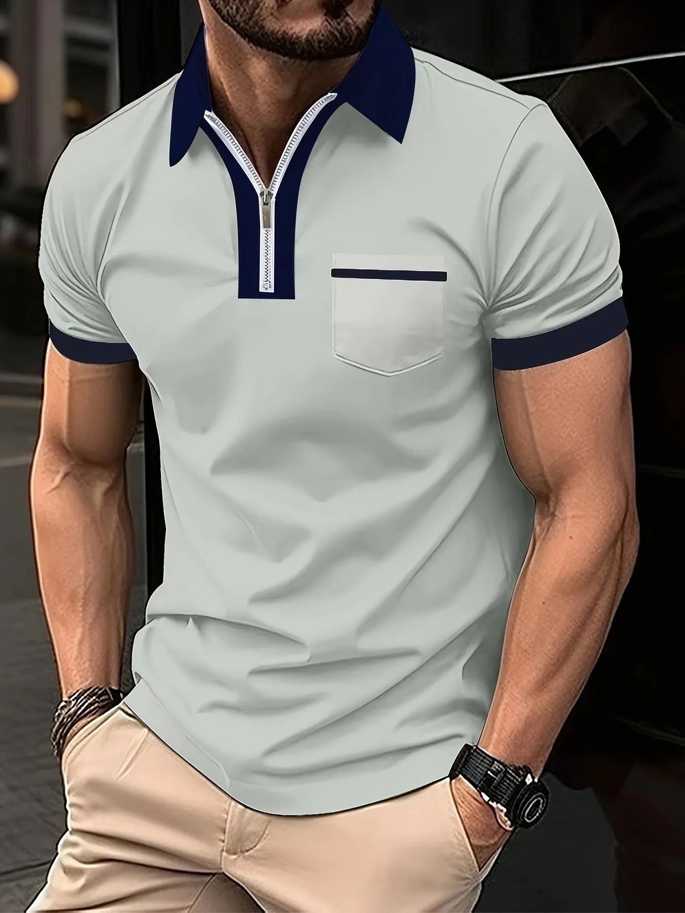 Man wearing a grey and navy blue casual t-shirt with a chest pocket and silver zip decoration detail.