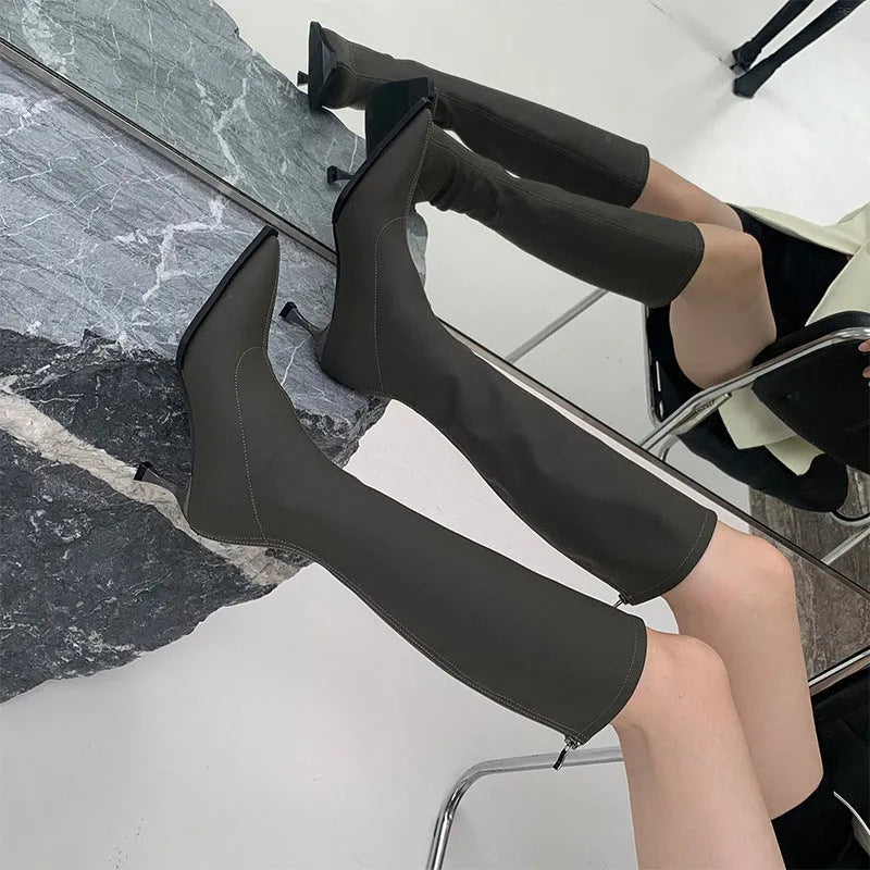 Black pointed toe women's below-the-knee boots with stiletto heel and back zipper fastening.