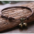 Black nylon rope dog collar with an attached brass bell lying on a wooden surface.