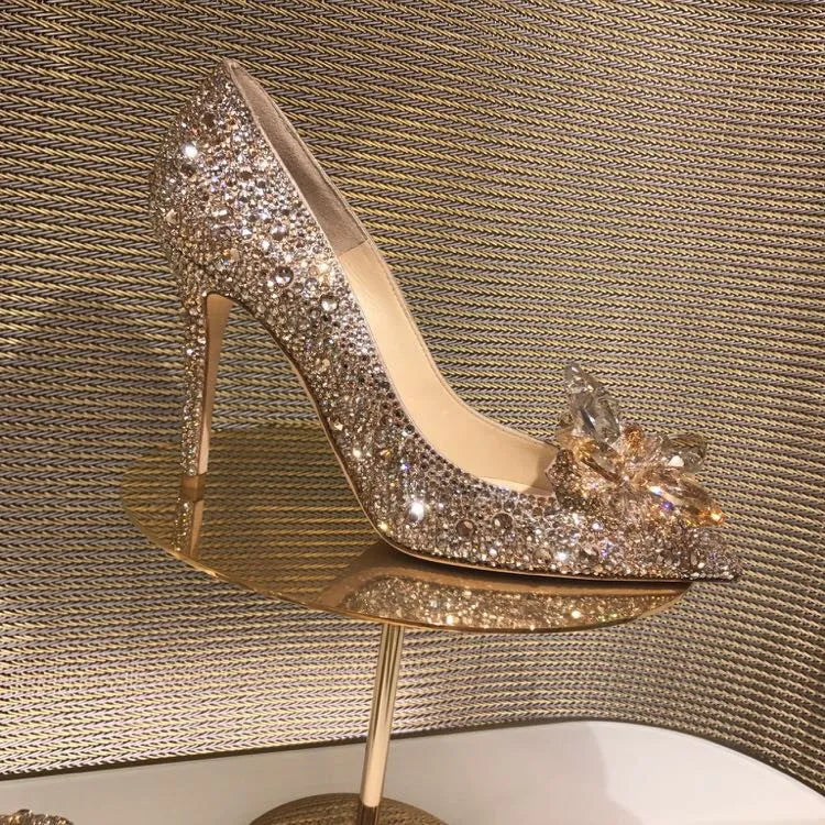 Gold women's high heels with pointed toe, rhinestone details, bow and stiletto heel on a plain background.