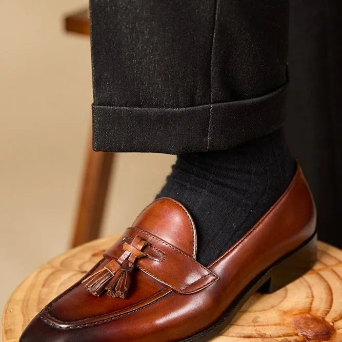 Men's black polished leather tassel loafers on a white background