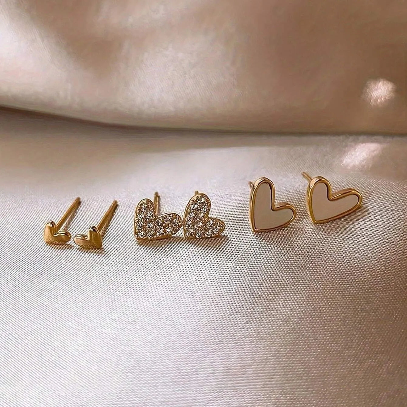 Set of three pairs of women's heart-shaped alloy drop earrings in gold, black, pink colours.