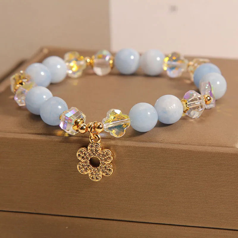 Women's aquamarine crystal bracelet with a four-leaf clover charm and a pearl accent on a model's wrist.