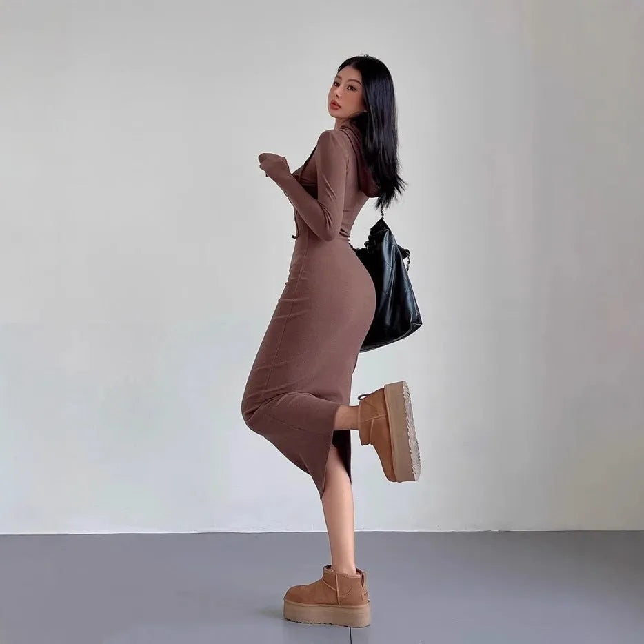 A woman wearing a grey high-waist hooded long sleeve sheath dress, knee-length pullover style.