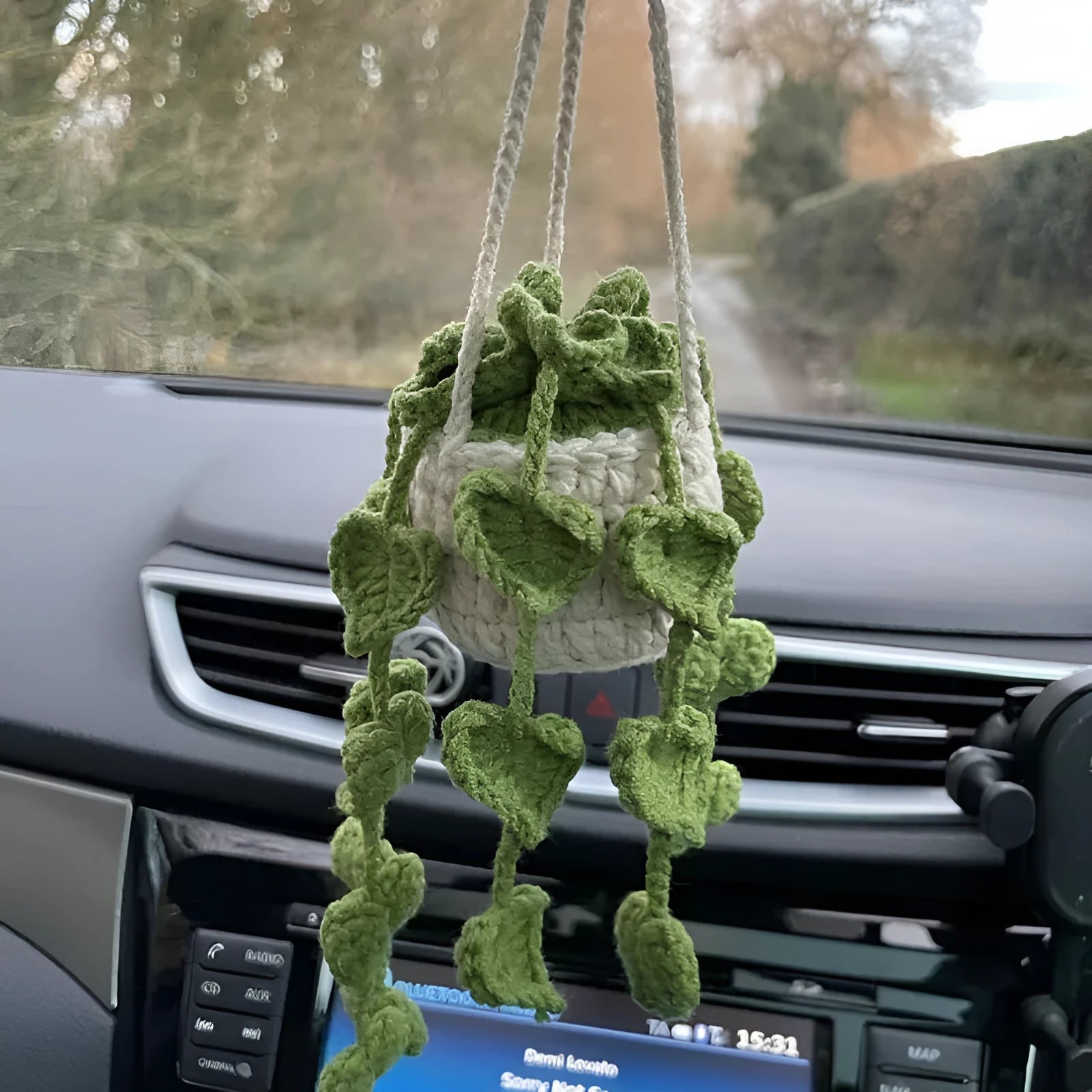 Green and white crochet wool car plant decoration with hanging rope on car dashboard