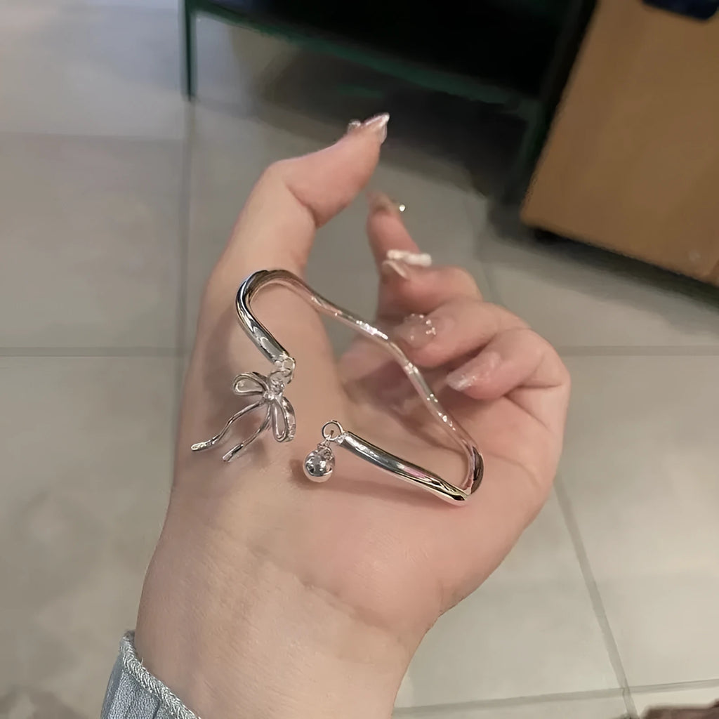 Silver adjustable bracelet with a bow charm and an opening bell charm on a model's wrist.