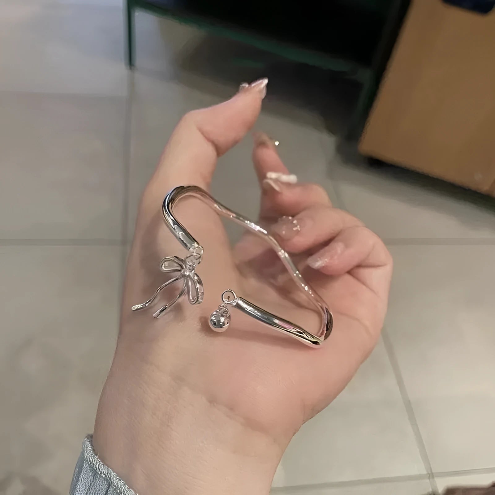 Silver adjustable bracelet with a bow charm and an opening bell charm on a model's wrist.