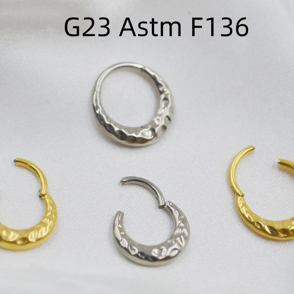 Close-up of a concave-convex carved titanium nose ring in gold finish on a grey background.