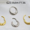 Close-up of a concave-convex carved titanium nose ring in gold finish on a grey background.