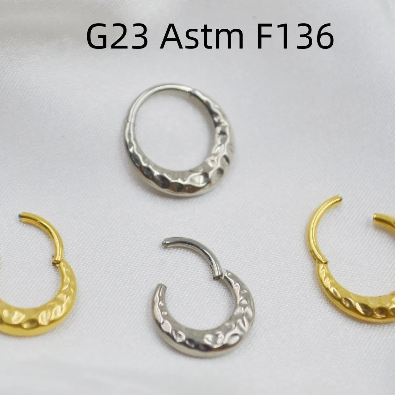 Close-up of a concave-convex carved titanium nose ring in gold finish on a grey background.