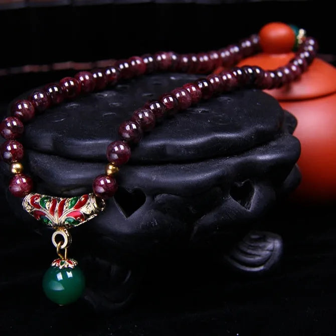 Close-up of a deep red natural garnet bracelet with 7mm beads, a golden toad charm, and a double ring clasp.