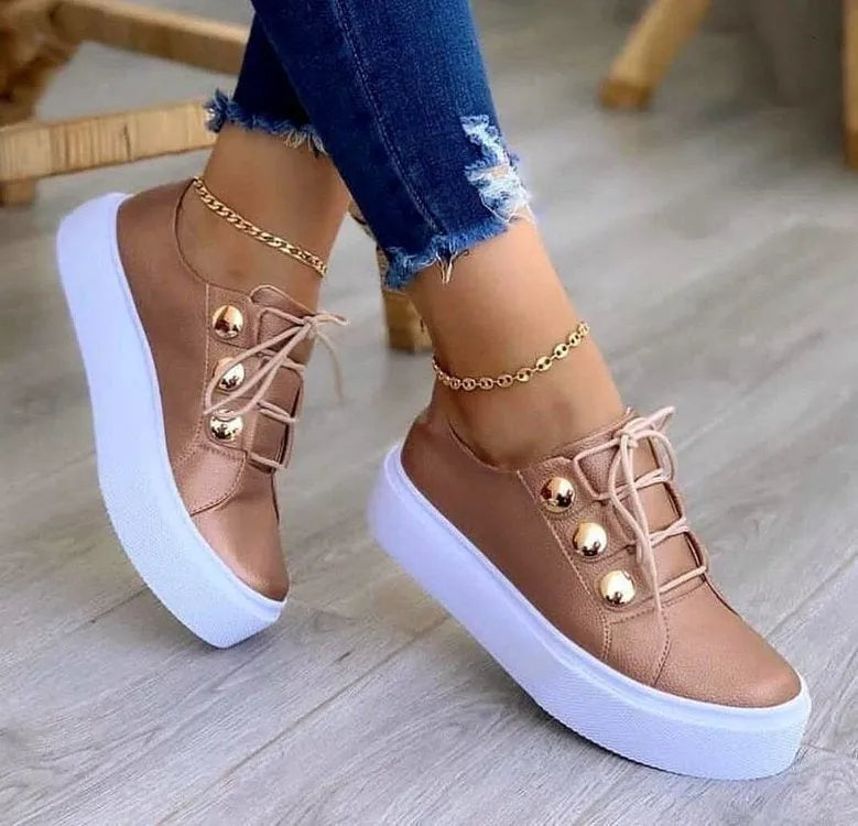 Women's white lace-up flats sneakers with silver rivet details on the low upper and a round toe.