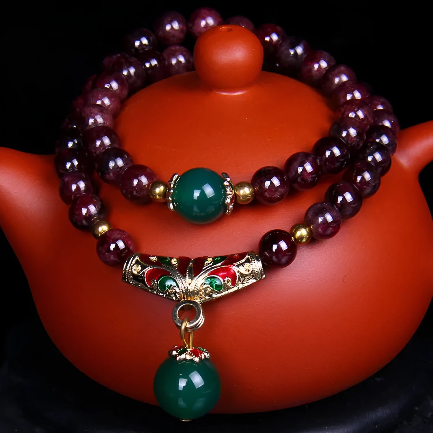 Close-up of a deep red natural garnet bracelet with 7mm beads, a golden toad charm, and a double ring clasp.
