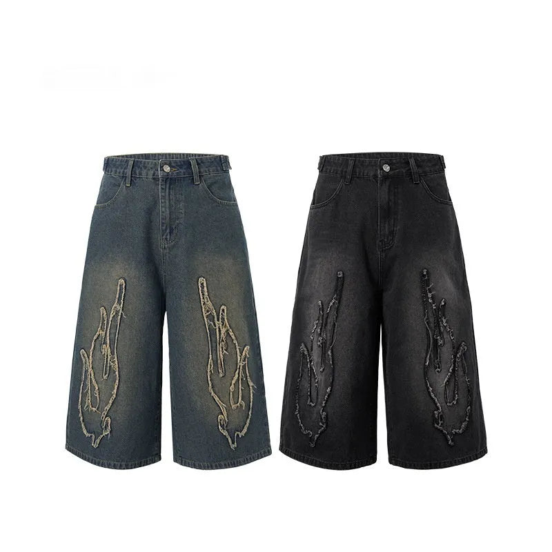 Men's black denim shorts with flame embroidery patches on the legs, showing a cropped, straight-leg cut.