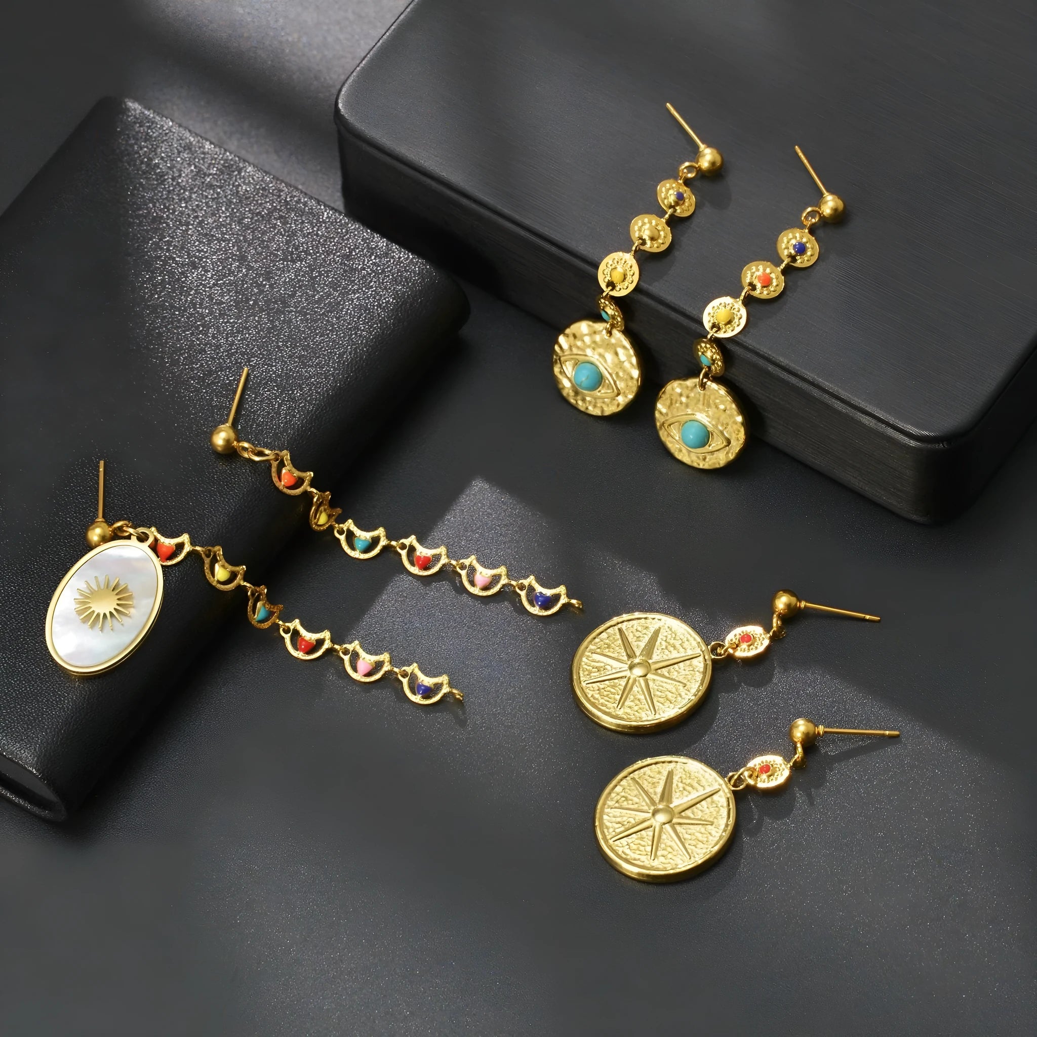 Three pairs of geometric stainless steel earrings: star, eye, and shell sun designs.
