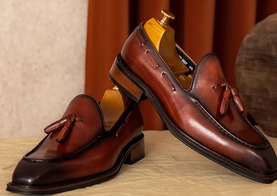 Men's black and brown British-style leather slip-on loafers showing polished leather upper and rubber sole