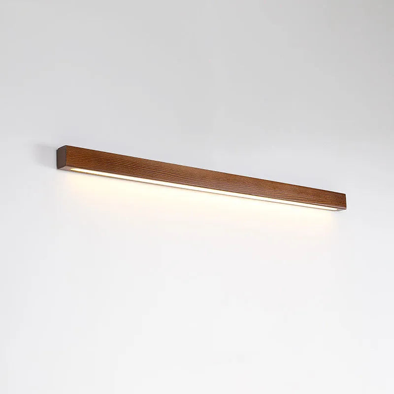 Slim walnut-coloured wooden strip LED wall lamp in three length options on a white wall.