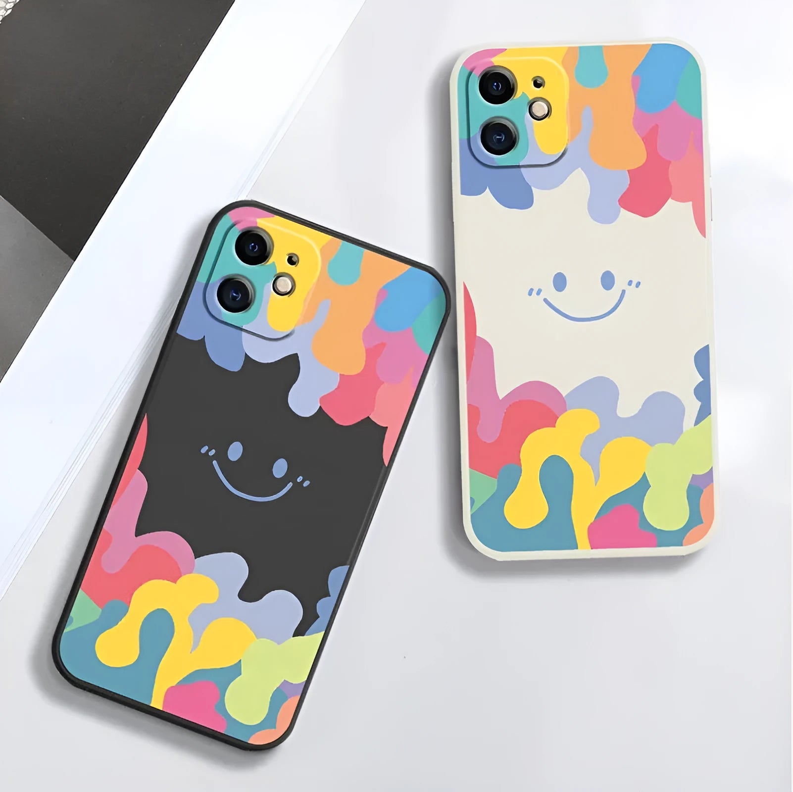 White and black silicone iPhone cases featuring a large rainbow smiley face design, shown with attached lanyards.