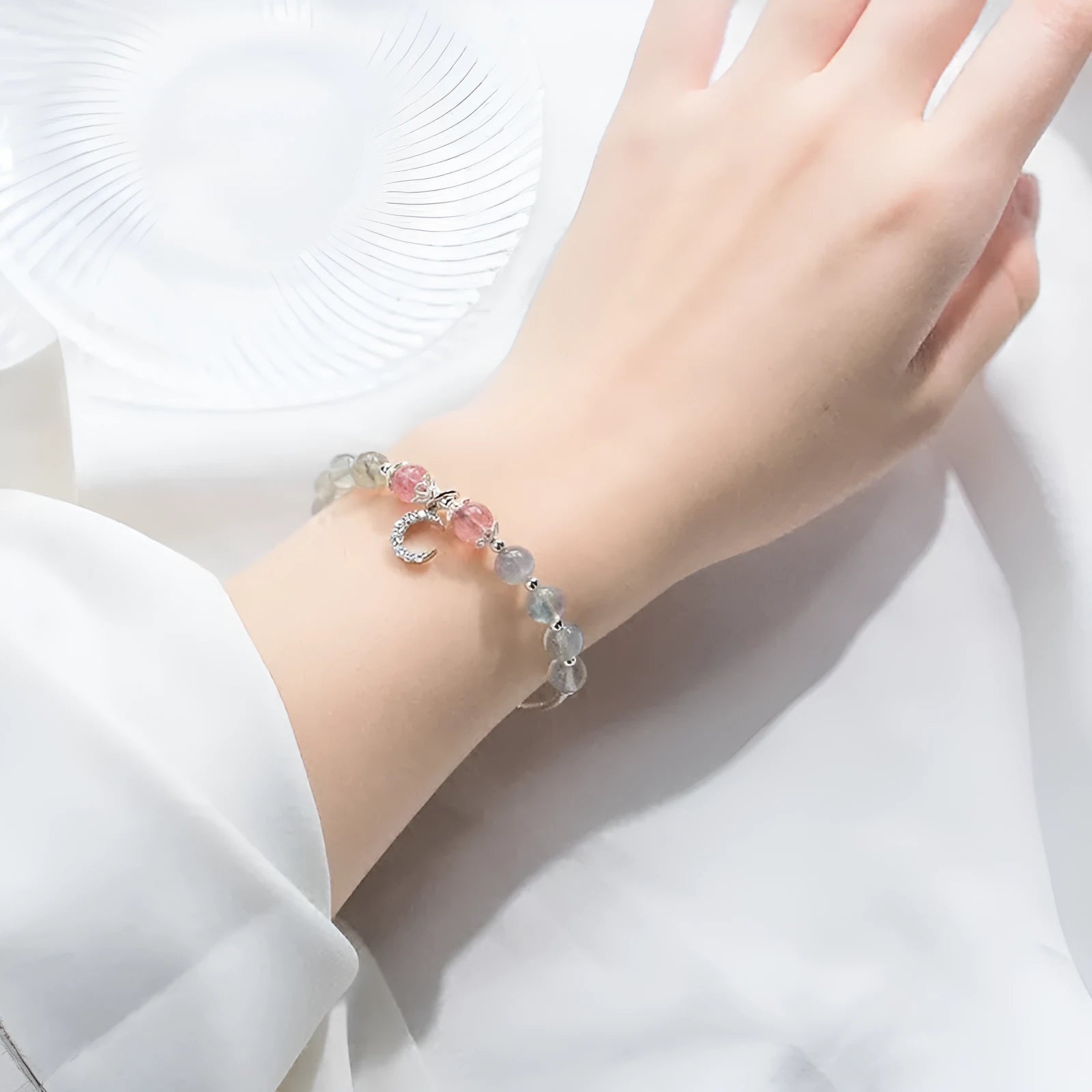 Natural moonstone bracelet with round beads, a crescent moon charm, and an adjustable silver chain on a wrist.