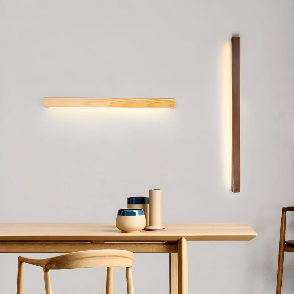 Slim walnut-coloured wooden strip LED wall lamp in three length options on a white wall.