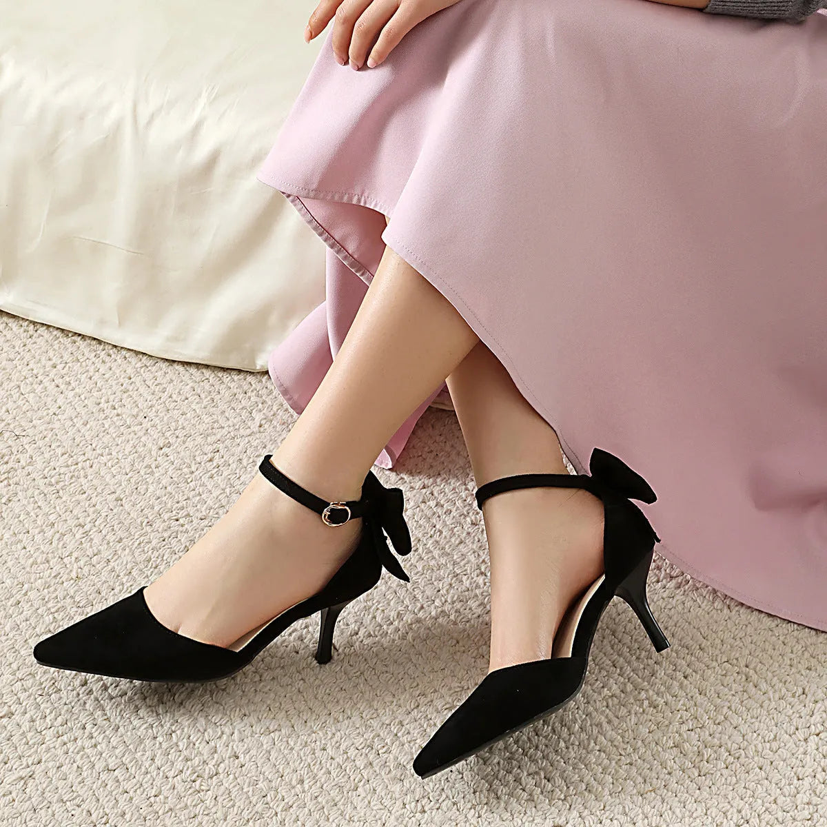 Black suede stiletto high heels with pointed toe, ankle buckle, and decorative bow knot.