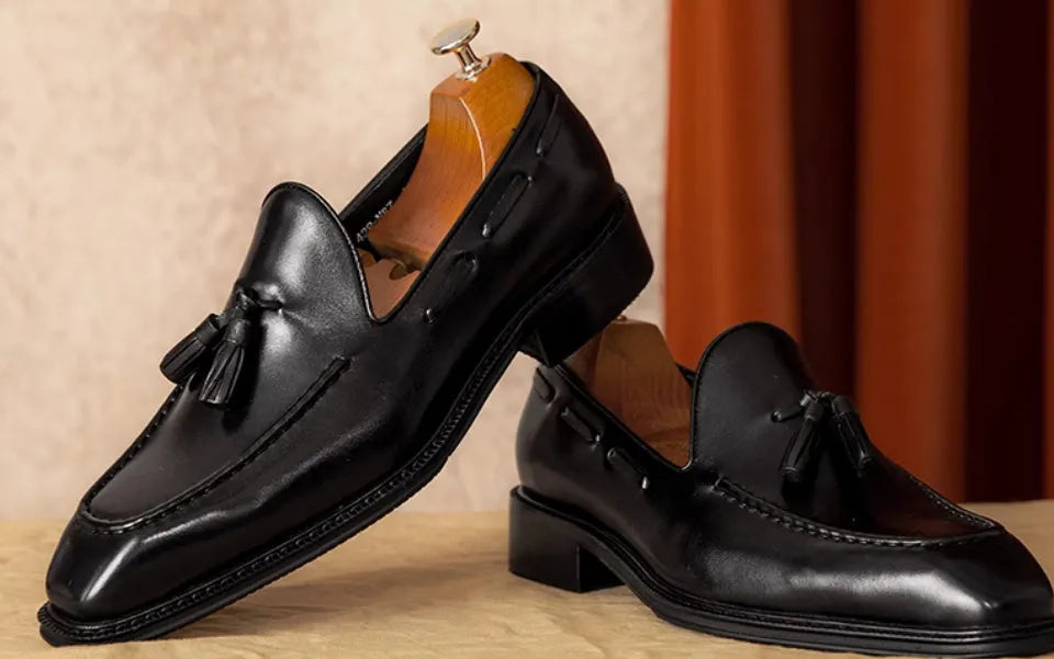 Men's black and brown British-style leather slip-on loafers showing polished leather upper and rubber sole