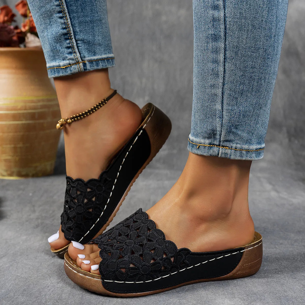 Women's black beach slippers with flower cutout design on the PVC upper and a rubber wedge sole.