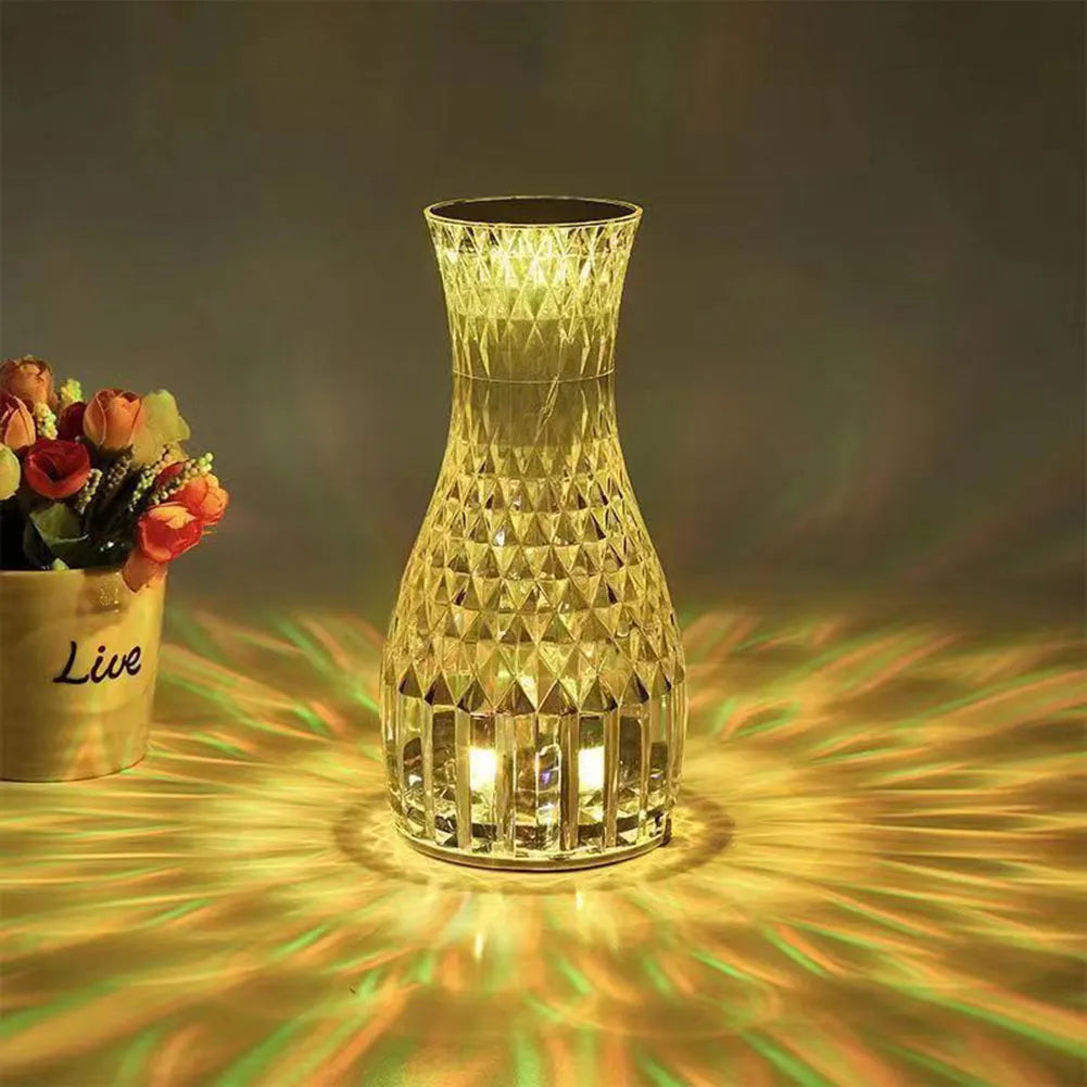 Clear plastic vase-shaped crystal bedside lamp with LED lights on a wooden table.