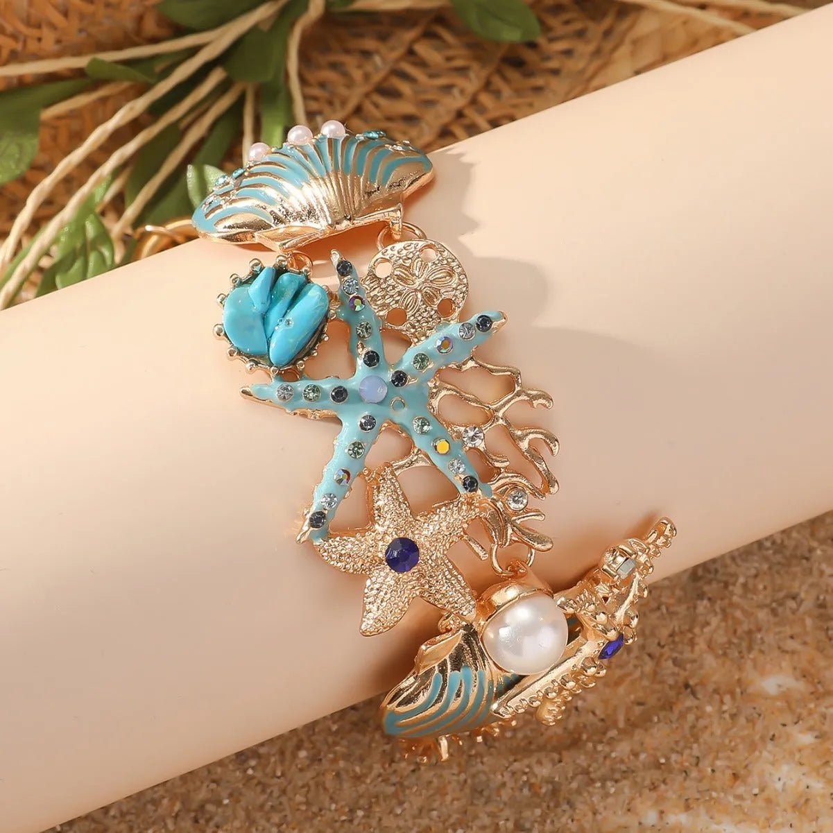 Close-up of a women's alloy bracelet featuring a boat anchor, marine shell, and starfish charms in a coral blue colour.