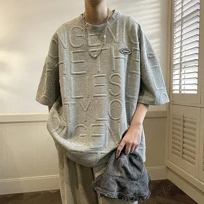 Men's grey loose-fit T-shirt with a raised white three-dimensional letter print on the chest.
